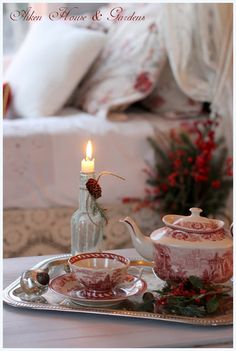 a tea set on a tray with a lit candle in the middle and christmas decorations around it