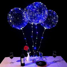 some balloons are on a table with wine glasses and a vase filled with red roses