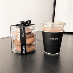 a cup of coffee next to a jar of cookies and a container of muffins