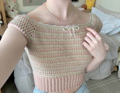 a woman wearing a pink and white knitted top is posing for the camera with her hands on her hips