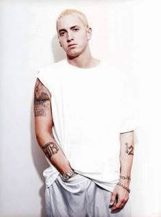 a man with tattoos on his arms and chest standing in front of a white wall