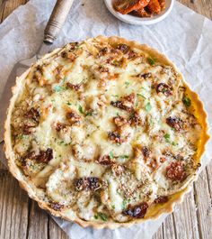 a pizza sitting on top of a wooden table next to a bowl of sauce and a fork