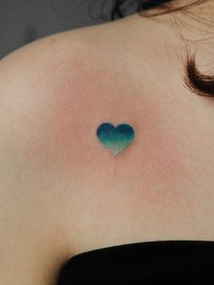 a small blue heart tattoo on the back of a woman's shoulder and chest