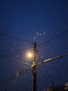 the street light is lit up at night time with snow falling all over it and power lines in the foreground