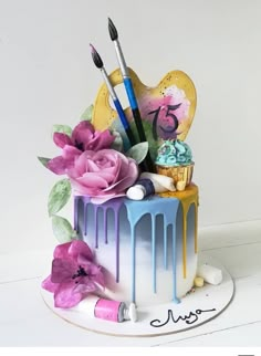 there is a cake decorated with paint and flowers on the top, as well as brushes