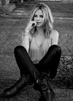 a woman sitting on the ground talking on a cell phone next to a chain link fence