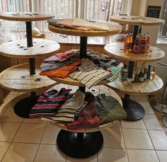 three tiered tables with shirts on them in a store display area next to a window