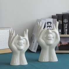 two white ceramic hands with faces are on a table next to books and a calendar