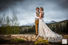 a bride and groom pose for a wedding photo in the mountains with their arms around each other