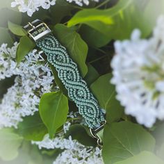 a green braided bracelet sitting on top of some white lilacs in the background