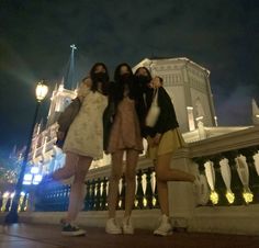 three young women standing next to each other in front of a white building at night