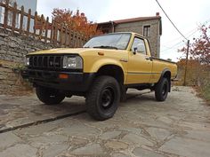 a yellow pick up truck parked in front of a stone wall and wooden fenced area