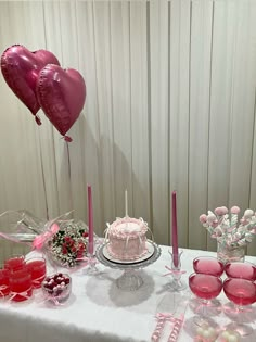 a table topped with a pink cake and two heart shaped balloons on top of it