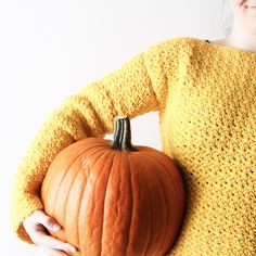 a woman is holding a pumpkin in her hands while wearing a knitted yellow sweater