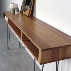 a wooden table with hairpin legs and a mirror on it's shelf next to a wall