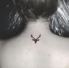 the back of a woman's neck with a small deer head tattoo on it