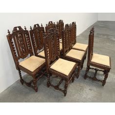 six carved wooden chairs with beige upholstered seats and back cushions in an empty room