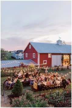 an outdoor event with people sitting at tables in front of a barn and red building