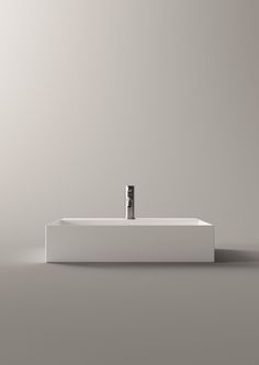 a white sink with a black faucet on it's side in front of a gray wall