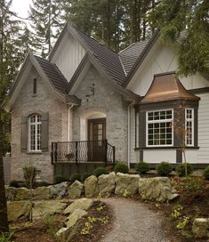 a house in the woods surrounded by trees and rocks with a walkway leading to it