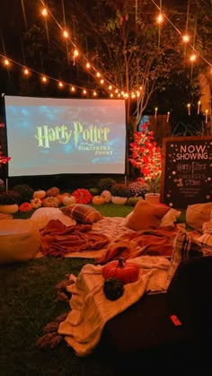 an outdoor movie is set up on the grass with lights strung over it and pumpkins