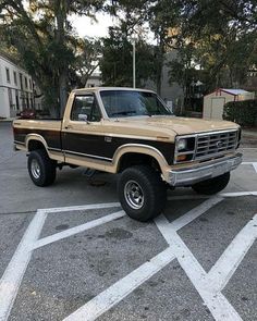 a tan and black truck parked in a parking lot next to some trees with white lines on the ground