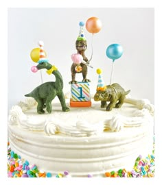 a birthday cake with two dinosaurs and balloons on it's top, in front of a white background