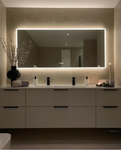 a bathroom with a large mirror above the sink and lights on the wall behind it