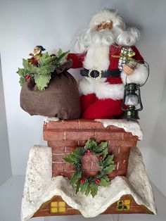 a santa clause figurine sitting on top of a brick chimney with wreaths