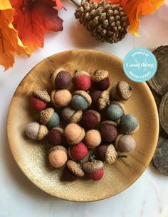 a wooden bowl filled with wool balls on top of a table next to autumn leaves