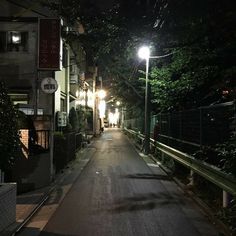 an empty street at night with lights on and trees lining the sides of the road