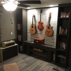 two guitars are hanging on the wall next to a guitar amplifier and bookcase in a living room