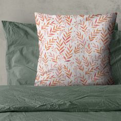 an orange and white pillow sitting on top of a bed next to green linens