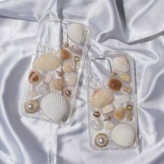 two cell phones with shells on them laying on a white satin surface, one is clear and the other is gold