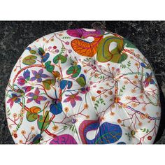 a colorfully decorated round seat cushion on a black granite surface with flowers and leaves painted on it