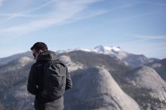 a man standing on top of a mountain talking on a cell phone with mountains in the background