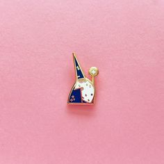 a lapel pin with a blue and white cat on it's head sitting on a pink surface