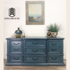 a blue dresser sitting in front of a painting and potted plant on top of it