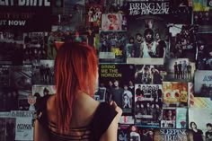 a woman with red hair standing in front of a wall full of posters and flyers