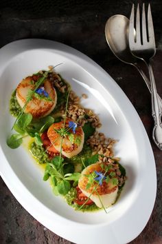 a white plate topped with scallops covered in greens and sauce next to a fork