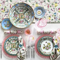 the table is set with pink and blue plates, silverware, and napkins