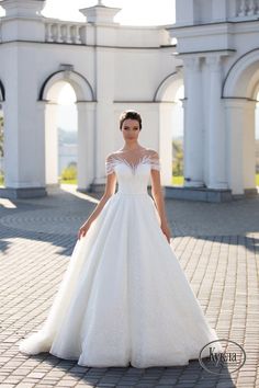 a woman in a white wedding dress standing on a brick walkway with an archway behind her