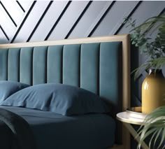 a bed with blue sheets and pillows next to a potted plant on a side table