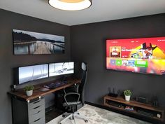 a desk with two monitors and a keyboard on it in front of a flat screen tv