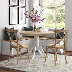 a dining room table with two chairs and a bench in front of a window that has pictures on the wall