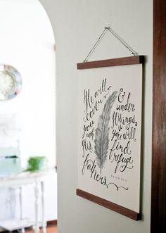 a wall hanging on the side of a room with a feather and bible verse written in cursive writing