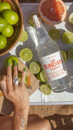 a person sitting at a table with limes, grapefruit and a bottle