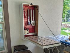 an outdoor table with two stools in front of it and some bottles hanging from the wall