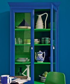 a green chair sitting in front of a blue bookcase filled with plates and cups