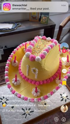 a yellow cake with pink frosting and sprinkles sitting on top of a table